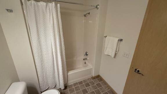 A white shower curtain hangs over a glass shower door in a bathroom.