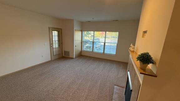 A room with a carpeted floor and a window with a view of the street.