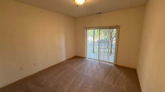 A room with a carpeted floor and a window with a view of a fence.
