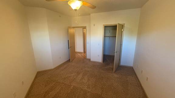 A carpeted room with a door and a ceiling fan.