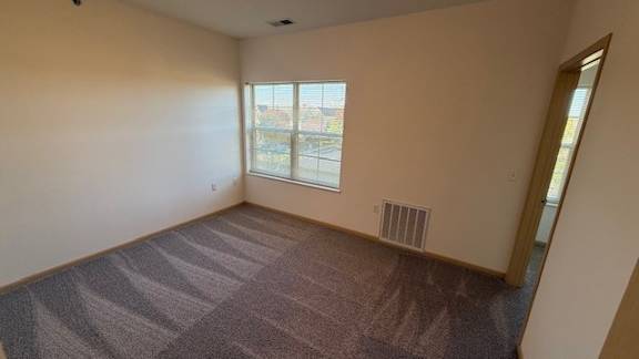 A room with a carpeted floor and a window overlooking a parking lot.