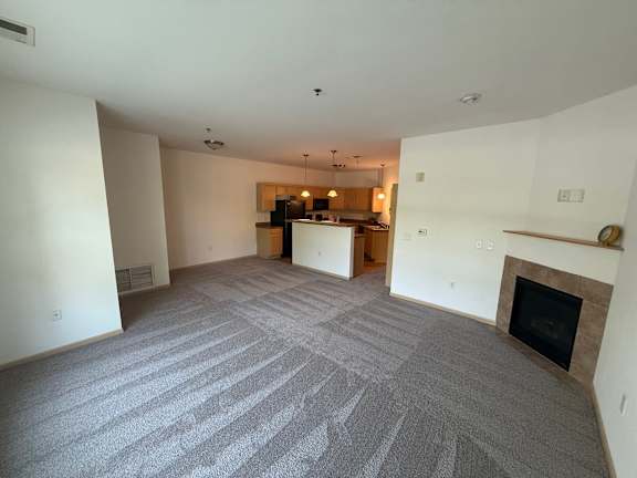 A large, empty living room with a fireplace and a kitchen in the background.