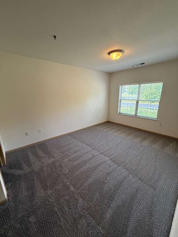 A room with a grey carpet and a window.