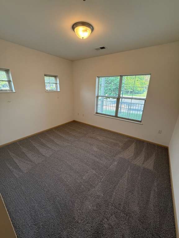 A room with a carpeted floor and two windows.