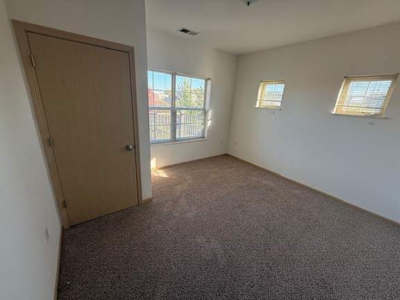 A room with a brown door, two windows, and carpeted floor.