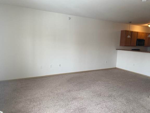 A room with a carpeted floor and a small kitchenette in the corner.