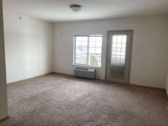 A room with a carpeted floor, a window with blinds, and a door leading to a balcony.