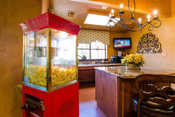 A inviting community refreshment area here at Tuscany at Faudree featuring a classic popcorn machine beside a granite countertop and bar seating. Warm lighting, decorative wall accents, and nearby sink and coffee station create a welcoming space for residents to gather, enjoy snacks, and relax indoors.