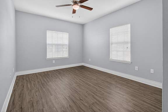 A room with a ceiling fan and two windows with blinds.