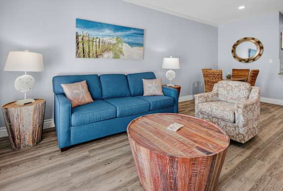A living room with a blue couch, two lamps, a wooden coffee table, and a painting on the wall.