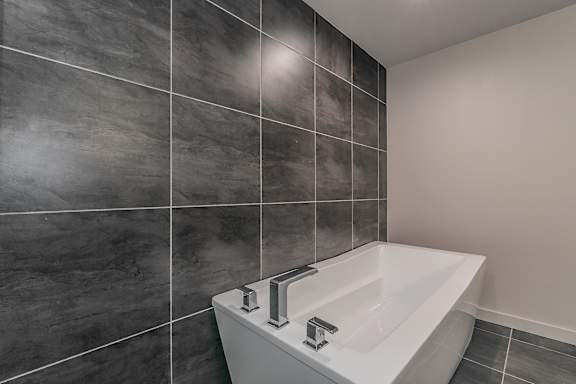 A white sink with chrome faucets in a bathroom with grey tiles.