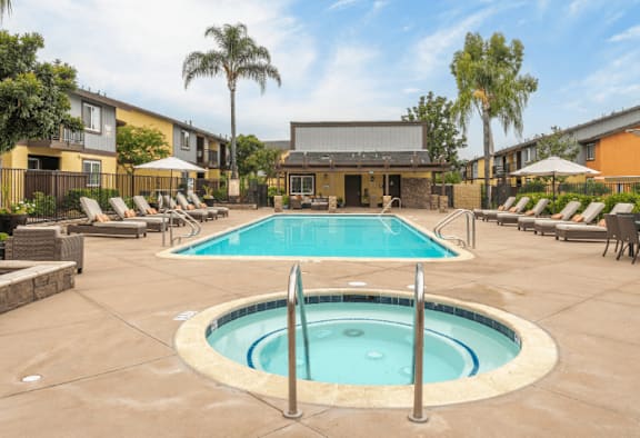 A large outdoor swimming pool surrounded by sun loungers and palm trees.