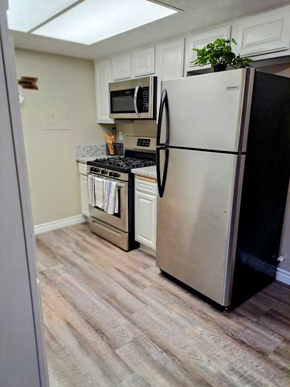 A stainless steel refrigerator stands in a kitchen with a stove and microwave in the background at Raintree Apartments, Highland, CA, 92346