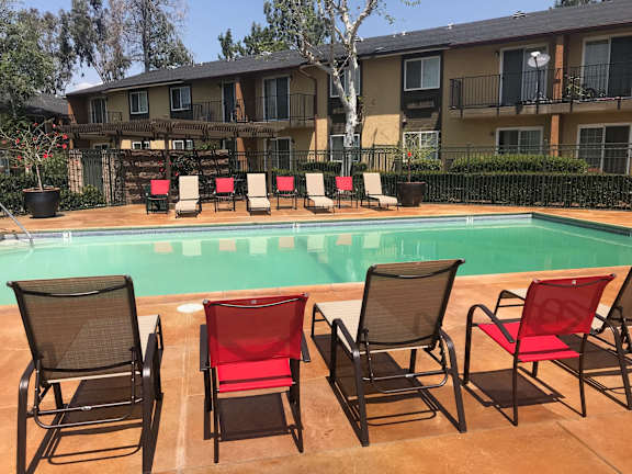 Bella Park apartment's pool surrounded by chairs and a building in the background in Rialto, California