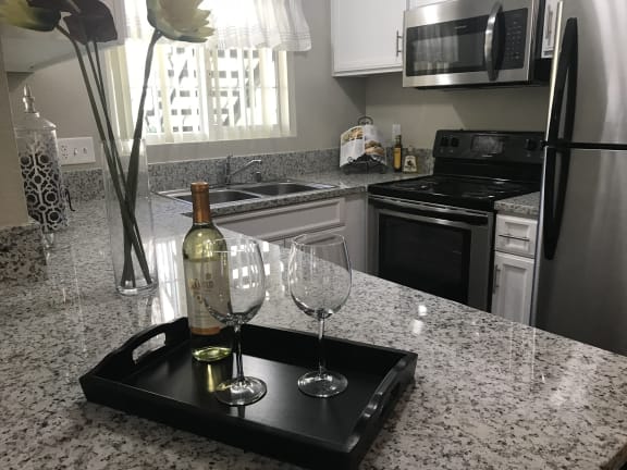 A black tray with a bottle of wine and two glasses on a granite countertop at Bella Park Apartments, Rialto, California
