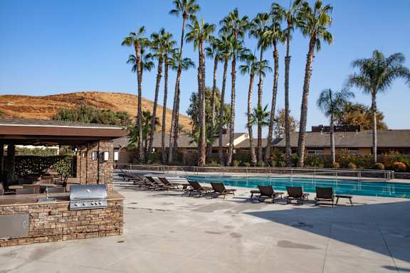 A pool surrounded by palm trees and a stone wall at Country Village Apartments, Jurupa Valley, CA 91752