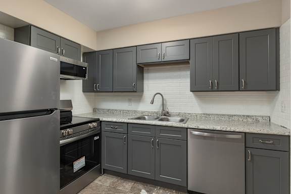 A kitchen with a stainless steel refrigerator and dark grey cabinets.