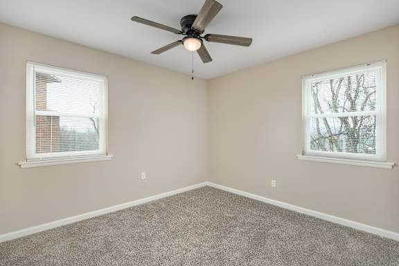 A room with a ceiling fan and two windows.