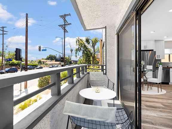 A balcony with a table and chairs overlooks a street with cars and traffic lights.