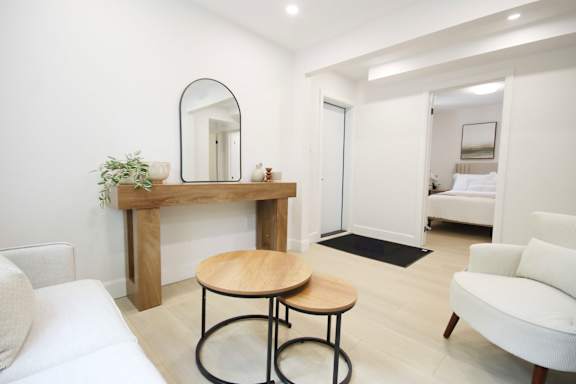 A white bedroom with a round table and a mirrored console table.