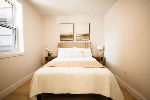 A bedroom with a bed, two lamps, and two pictures on the wall.