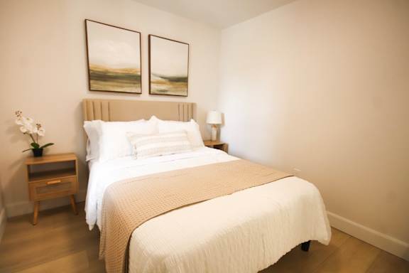 A bedroom with a large bed and two framed pictures on the wall.