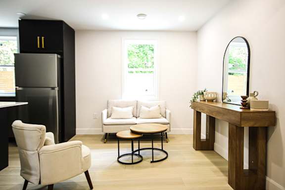 A black refrigerator stands next to a white chair in a room with a round table and a mirror.