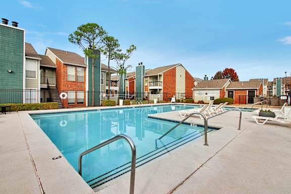 A swimming pool surrounded by a concrete floor and metal railings with apartment buildings in the background.