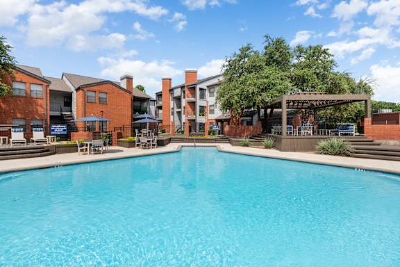 A large swimming pool in front of a building with a patio area.