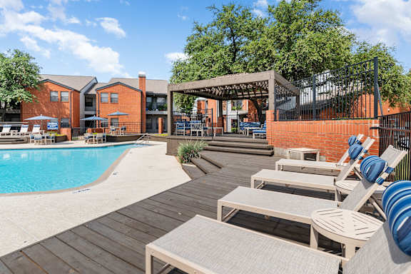 A pool area with sun loungers and a building in the background.