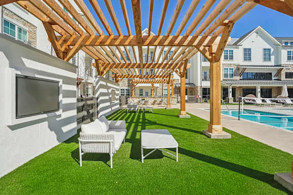 a backyard with a pool and a wooden pergola with chairs and a television