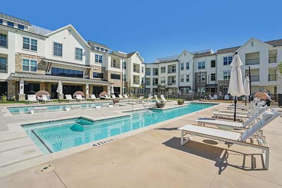 a swimming pool with lounge chairs and umbrellas in front of an apartment building