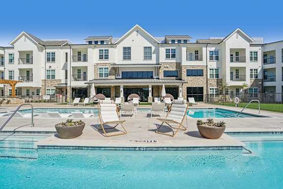 an outdoor pool with chairs and a building in the background