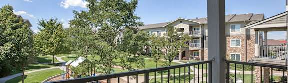 A balcony overlooks a tree-lined street and apartment buildings.