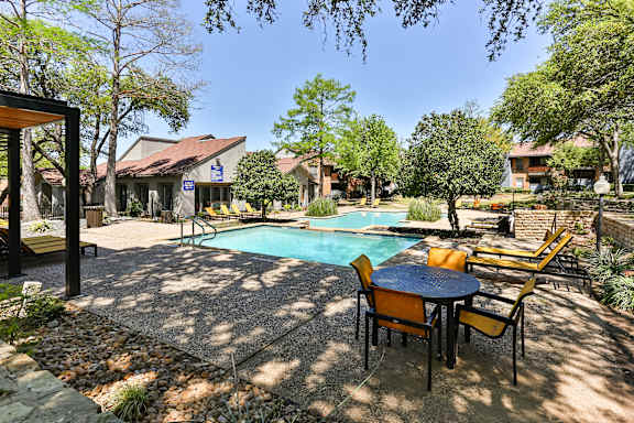 A pool surrounded by chairs and trees.