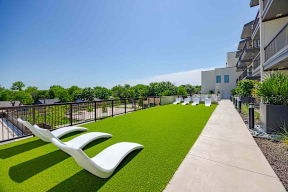A row of white chairs are lined up on a green lawn.