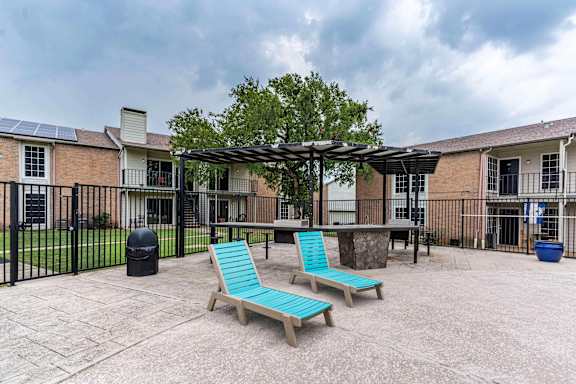 A patio with two chairs and a table is surrounded by a black fence.