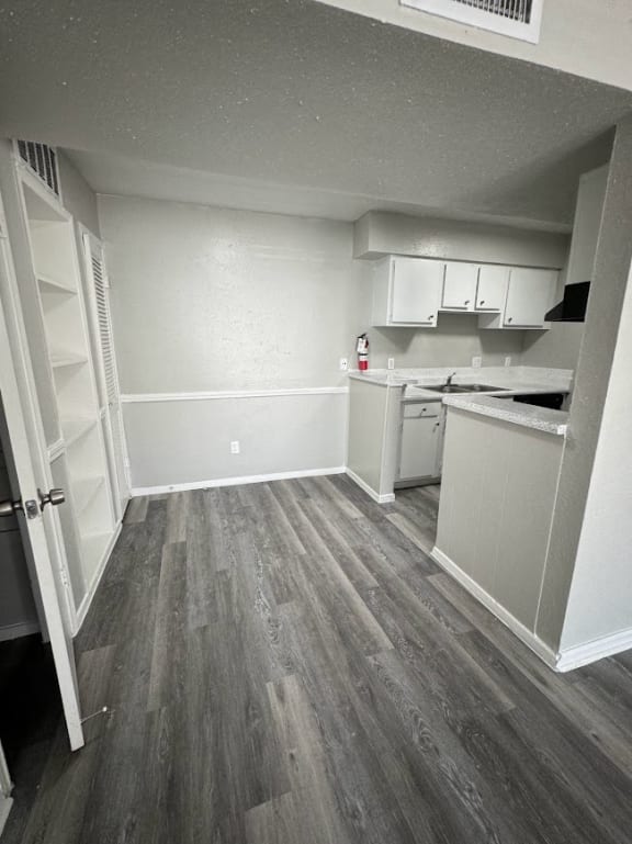 an empty kitchen with wooden floors and white cabinets
