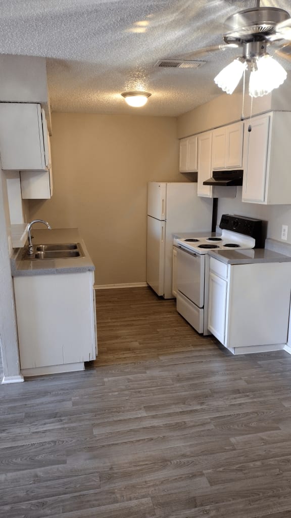 an empty kitchen with white appliances and a wood floor