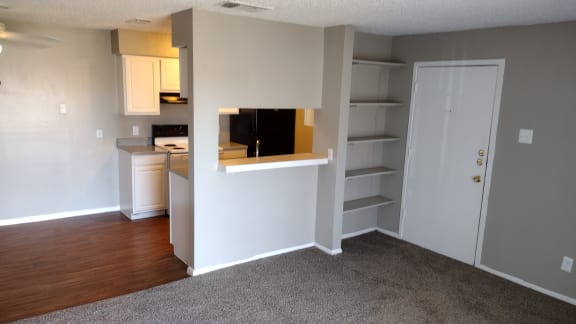an empty living room with an open window and a kitchen