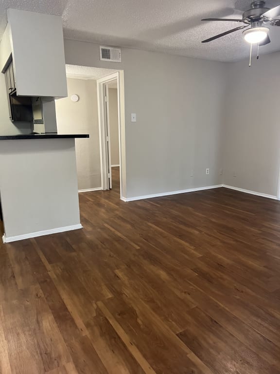 an empty living room with wood floors and a kitchen