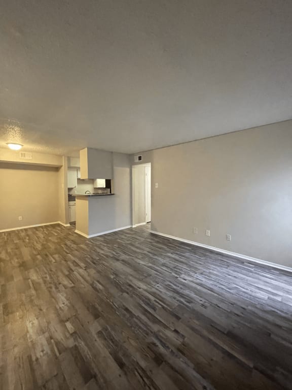 an empty living room with wood floors and a kitchen