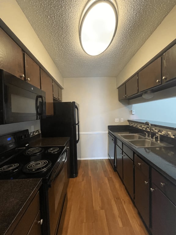 a kitchen with black appliances and wood flooring and a window