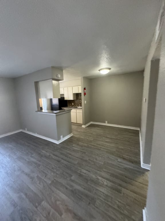 an empty living room with wood floors and a kitchen