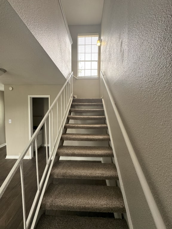 the stairwell of a house with carpeted stairs and a window
