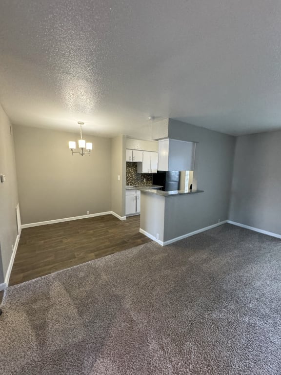 an empty living room with a kitchen in the corner