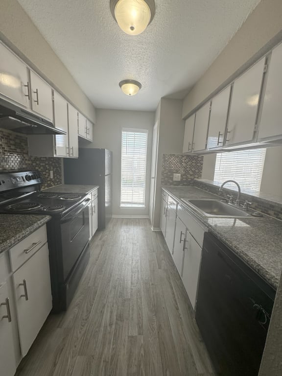 an empty kitchen with white cabinets and black appliances and a window