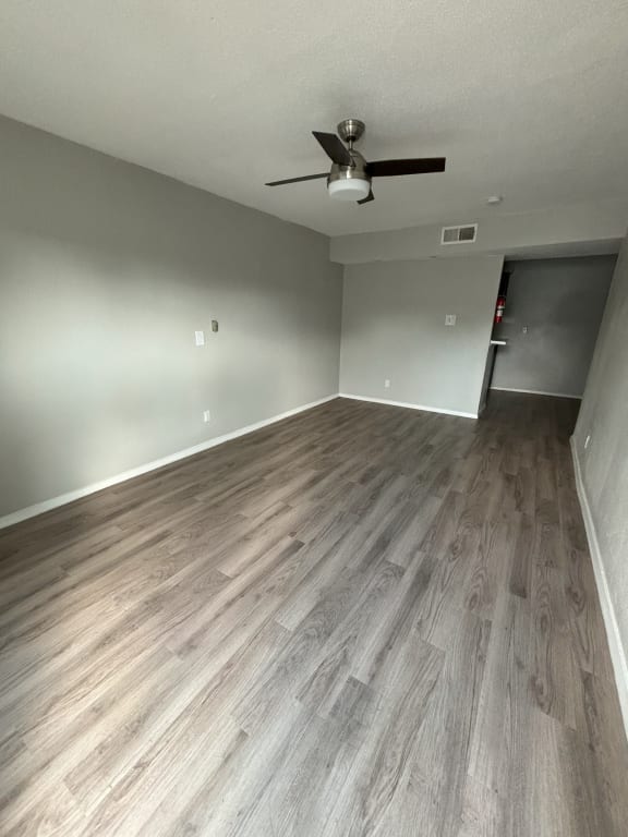 an empty living room with wood floors and a ceiling fan
