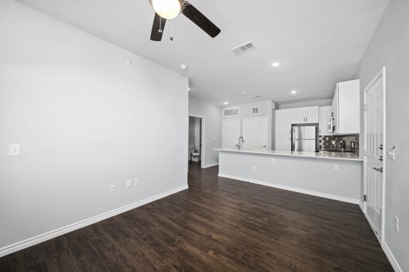 an empty living room and kitchen with white walls and wood flooring