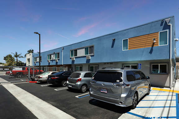 A silver car is parked in a parking lot in front of a blue building.